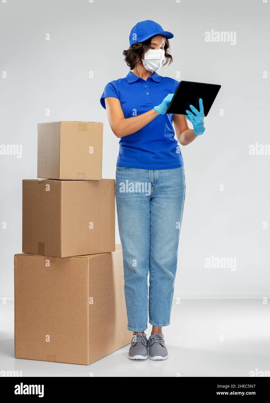 delivery woman in mask with boxes and tablet pc Stock Photo - Alamy