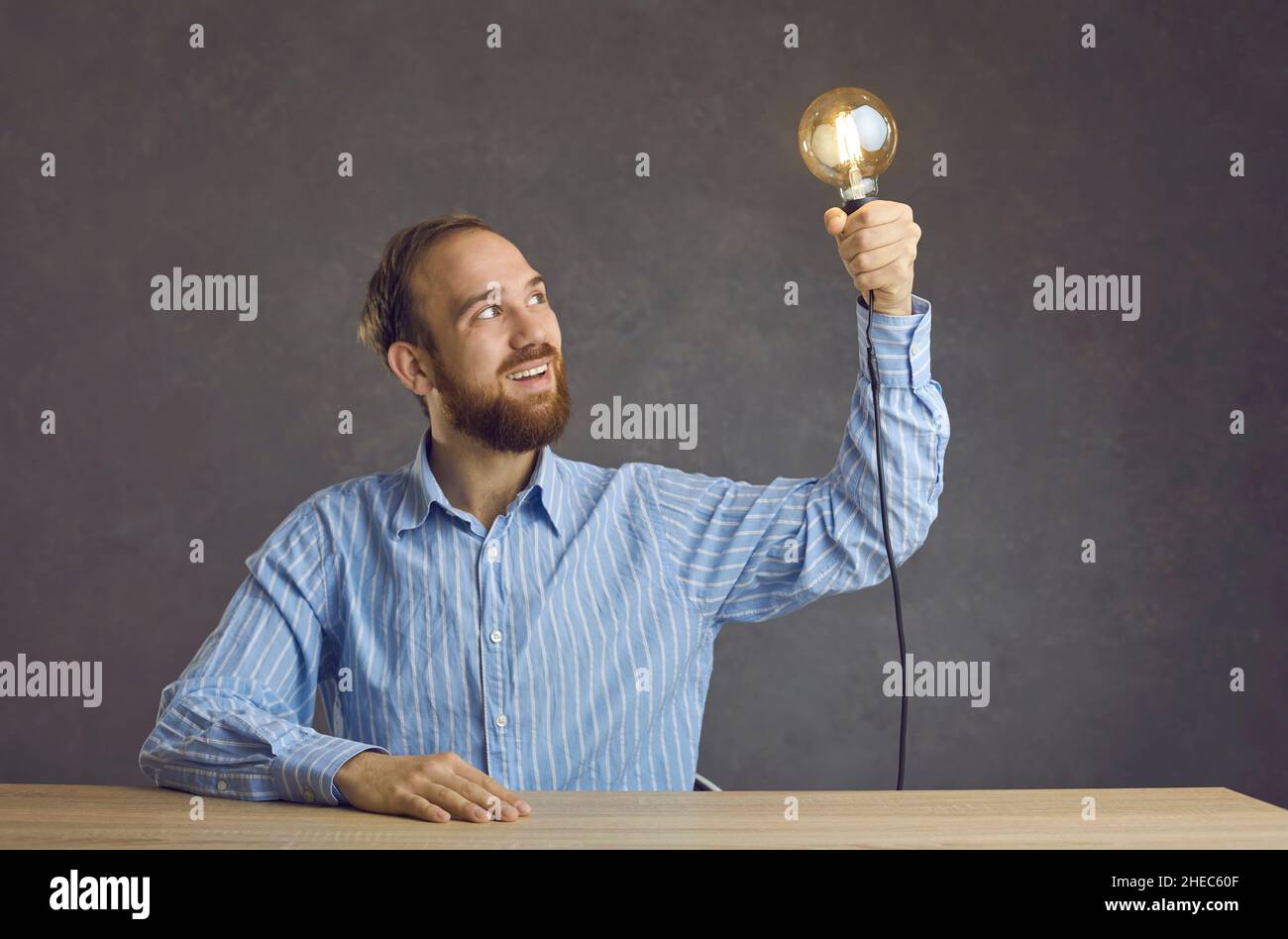 Portrait of excited man holding glowing bulb looking at light sitting at desk Stock Photo