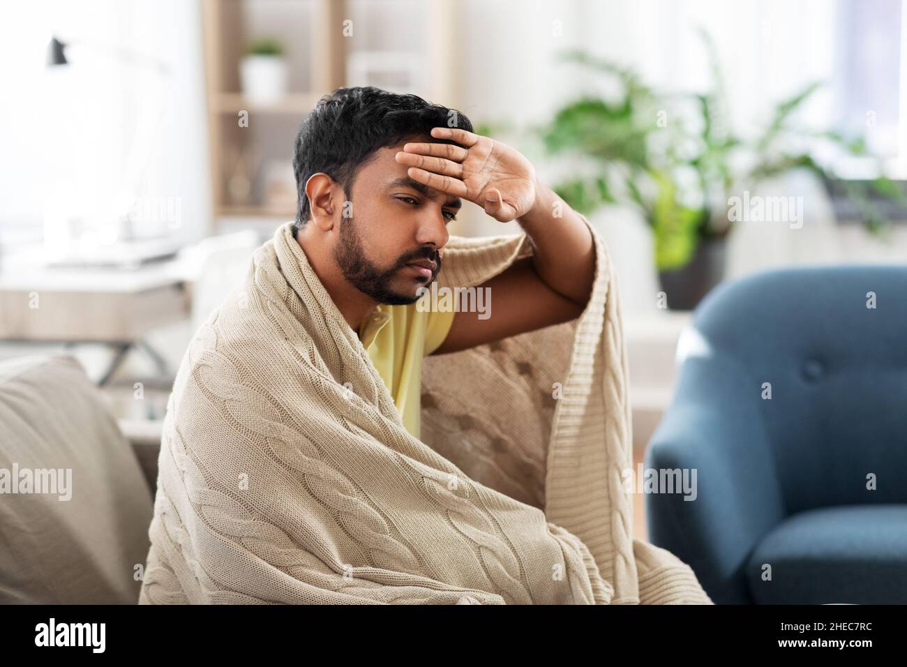 sick young man in blanket having headache or fever Stock Photo