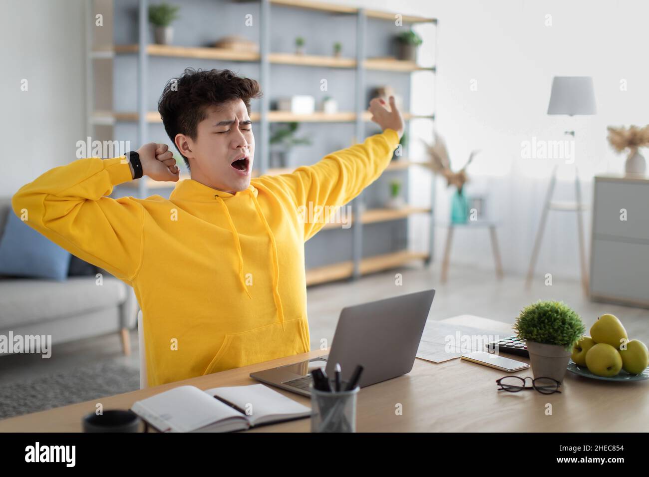 Asian male student yawning sitting at desk with pc Stock Photo - Alamy