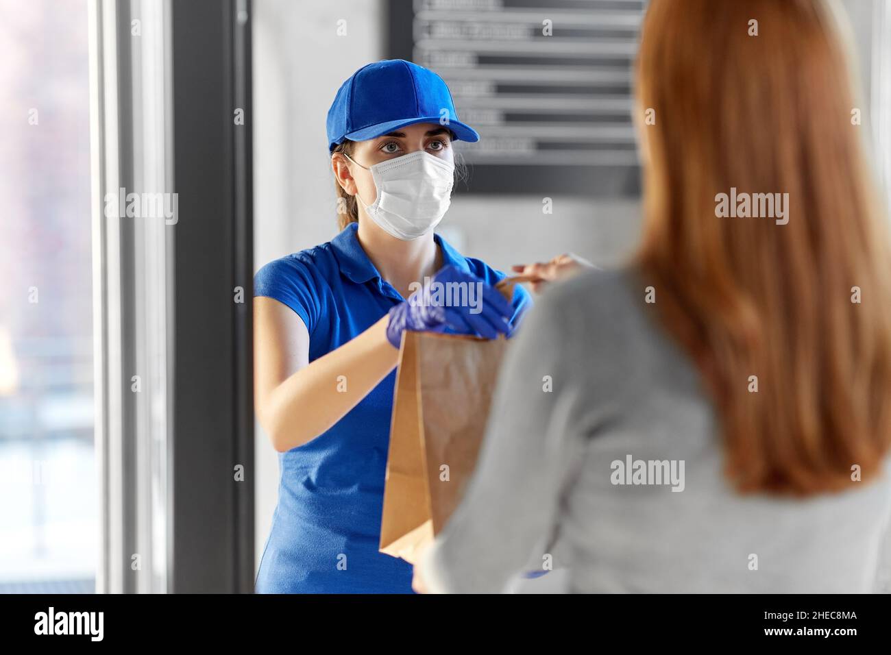 delivery girl in mask giving paper bag to woman Stock Photo - Alamy