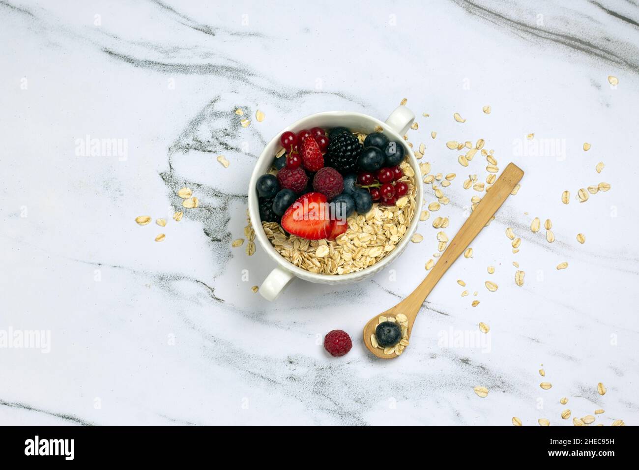 Healthy breakfast, oat with berry and wooden spoon on white marble table. top wave, flat lay. Stock Photo