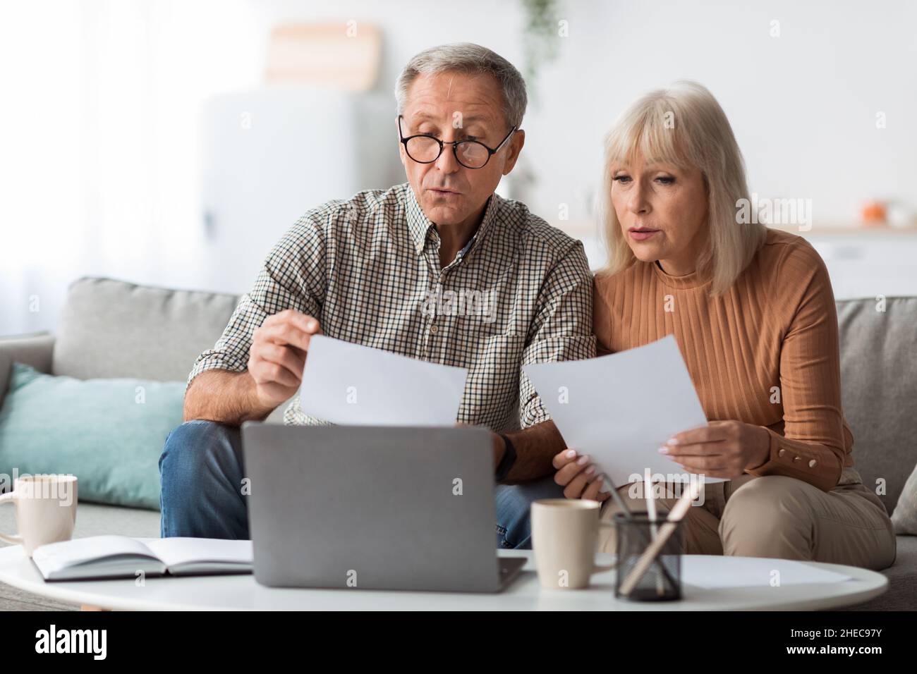 Senior Spouses Reading Papers And Bills Sitting Near Laptop Indoors Stock Photo