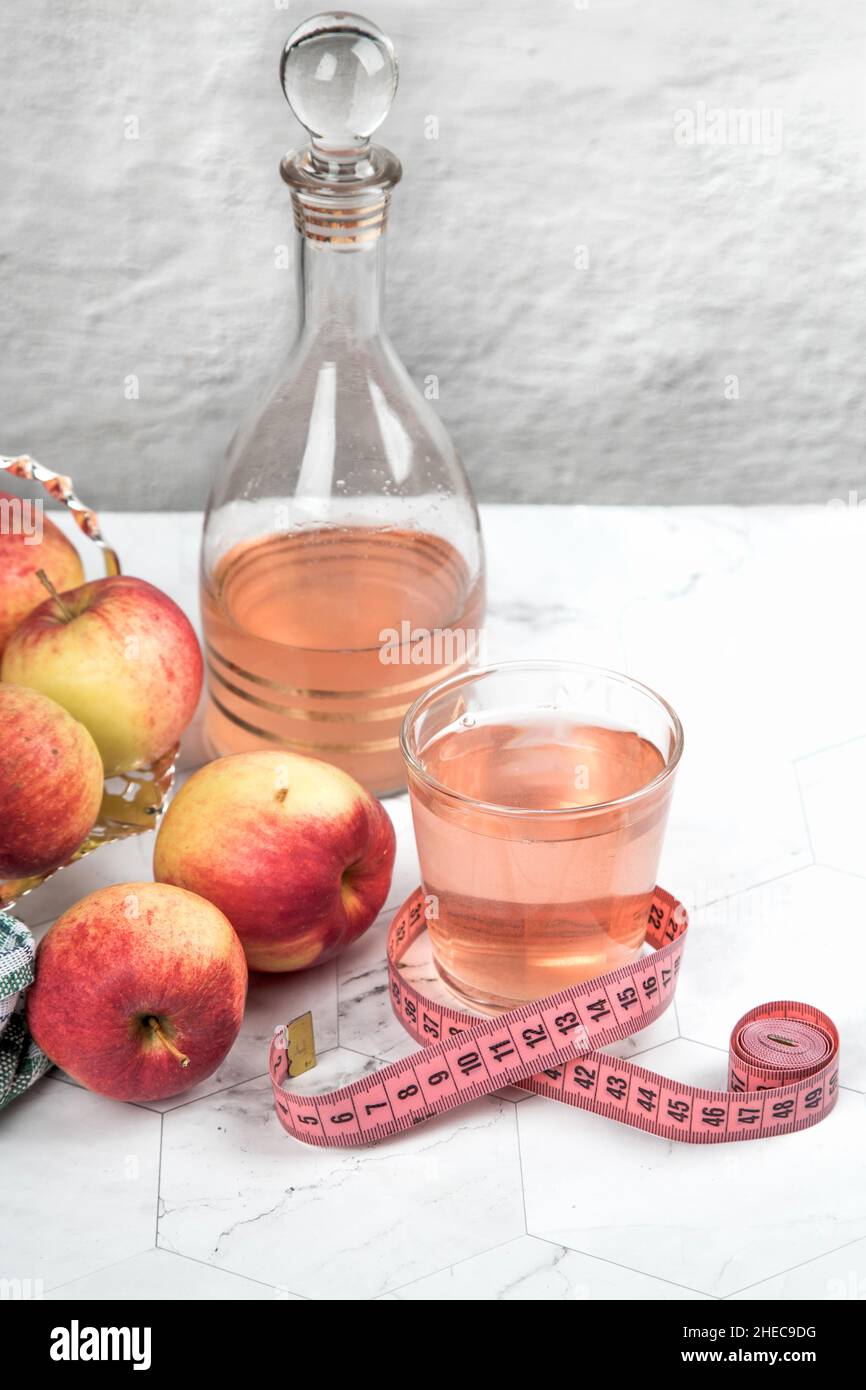 A glass with a measuring tape and a carafe of apple cider vinegar on a light table. The concept of weight control Stock Photo