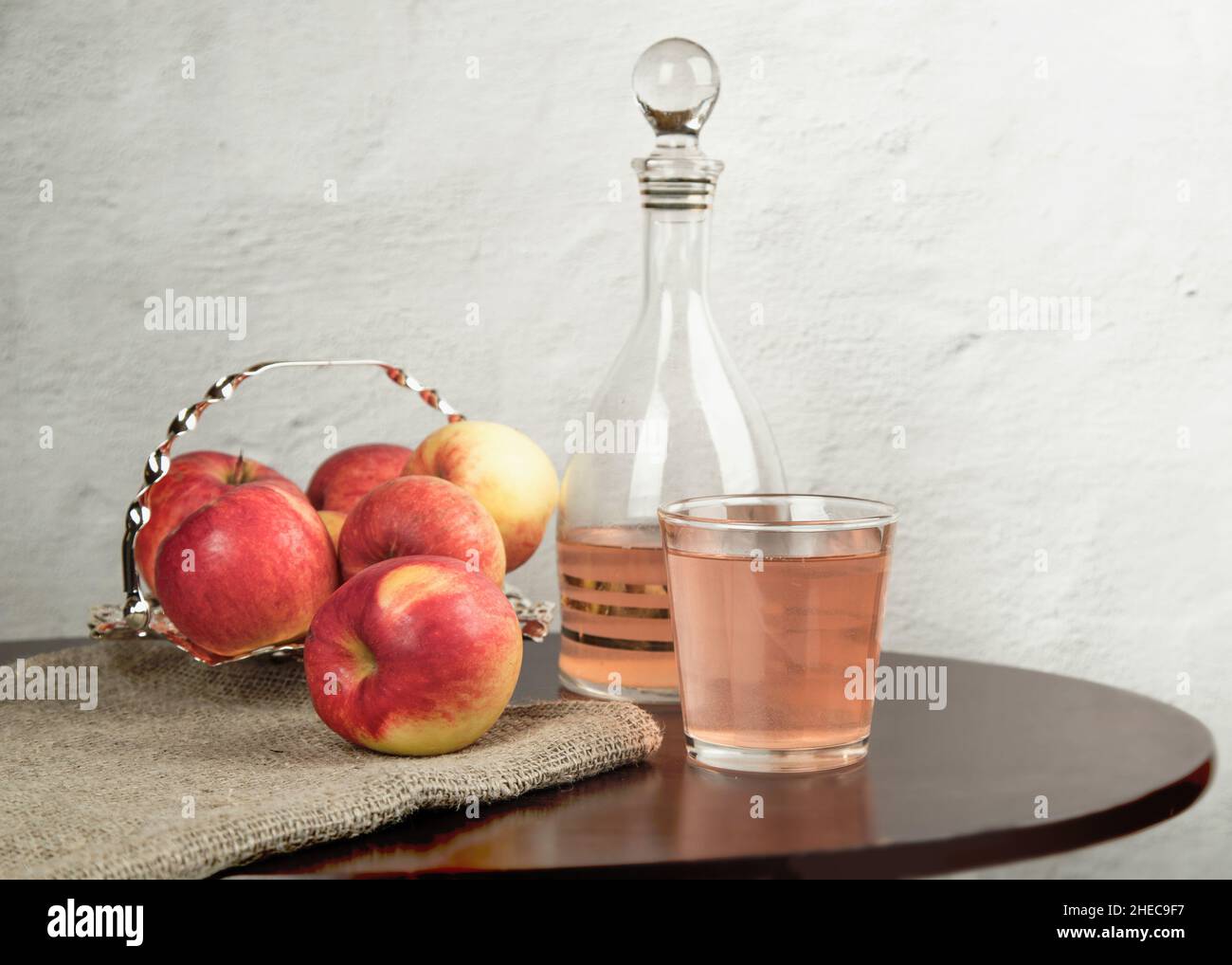 A glass and a decanter with apple cider vinegar on a light table against the background of a concrete wall. The concept of weight control Stock Photo