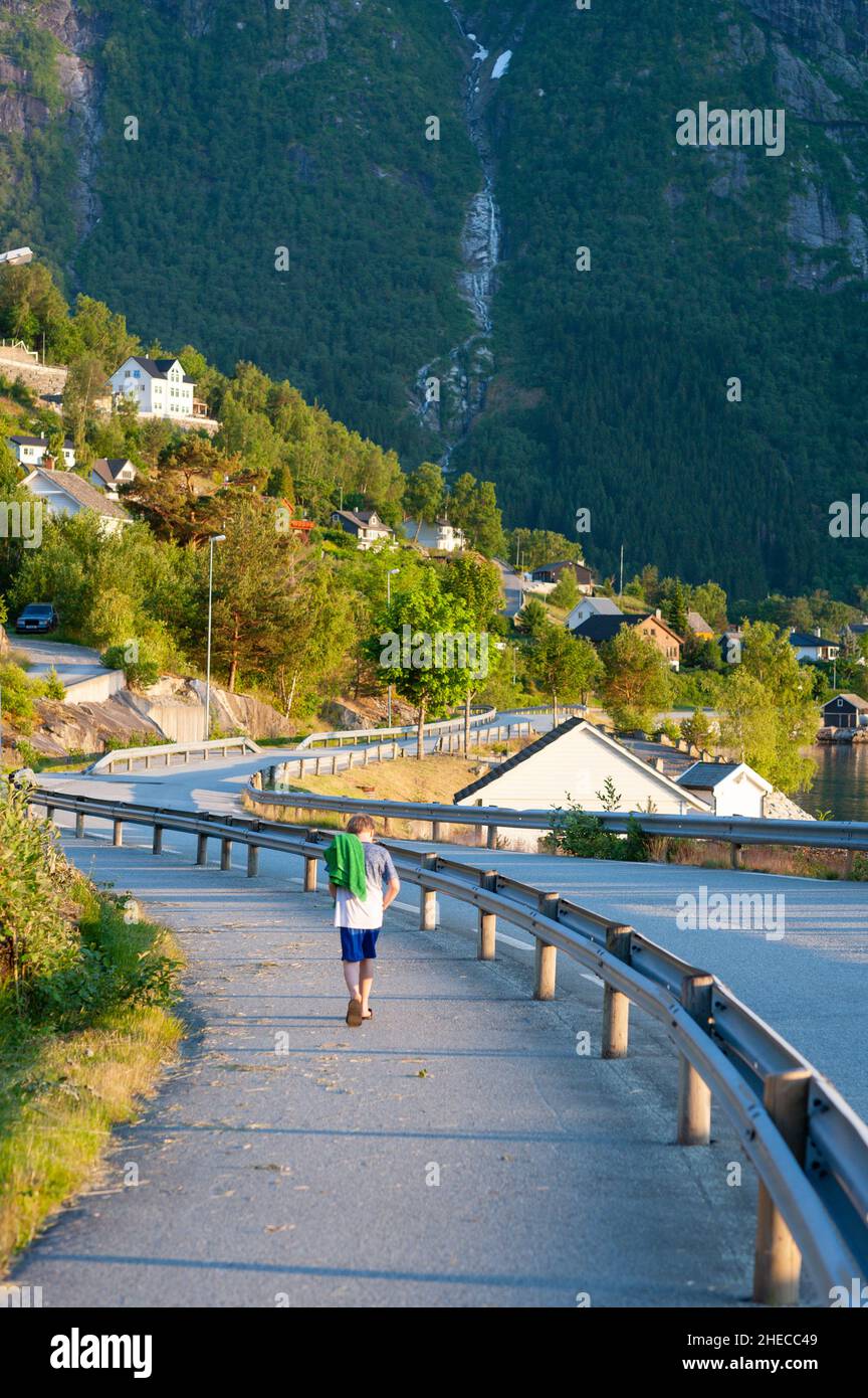 Child with towel walking along a coastal road, Eidfjord, Norway Stock Photo