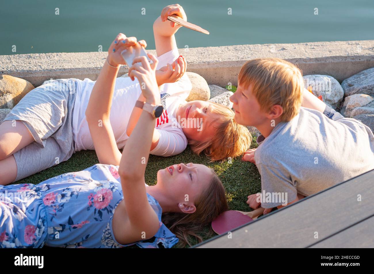 Kids with smart phones out on the deck by the sea enjoying warm sunlight, Eidfjord, Norway Stock Photo