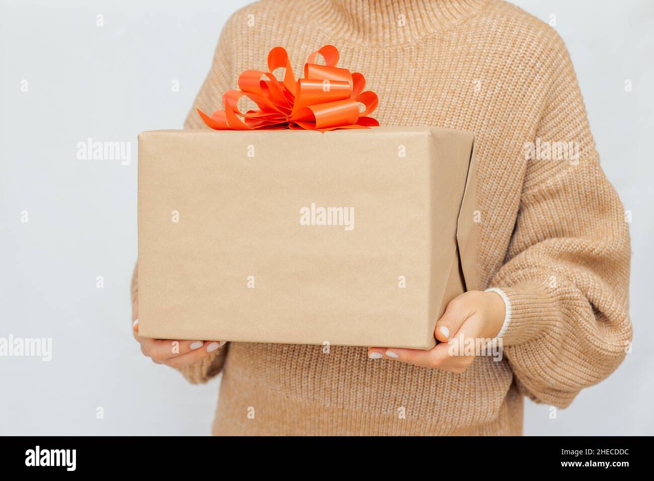 Woman's hands gift box with red ribbon. woman in warm beige jumper Hold present box with bow.  Stock Photo