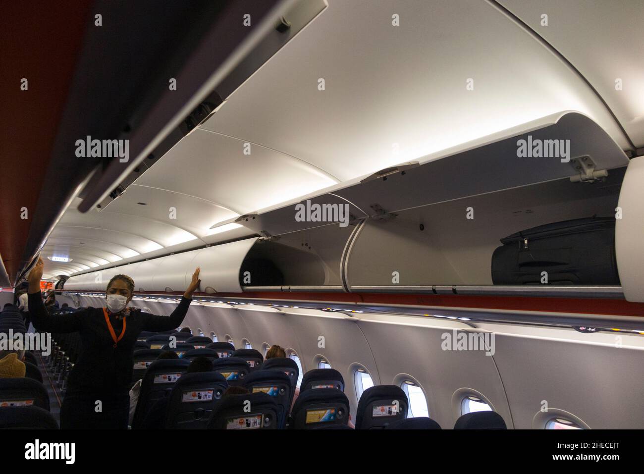 Member of cabin crew closing the doors on overhead passenger locker / lockers / compartment / compartments for stowing passengers bags cabin luggage, on an Easyjet Airbus A320 or A319 plane.  (128) Stock Photo