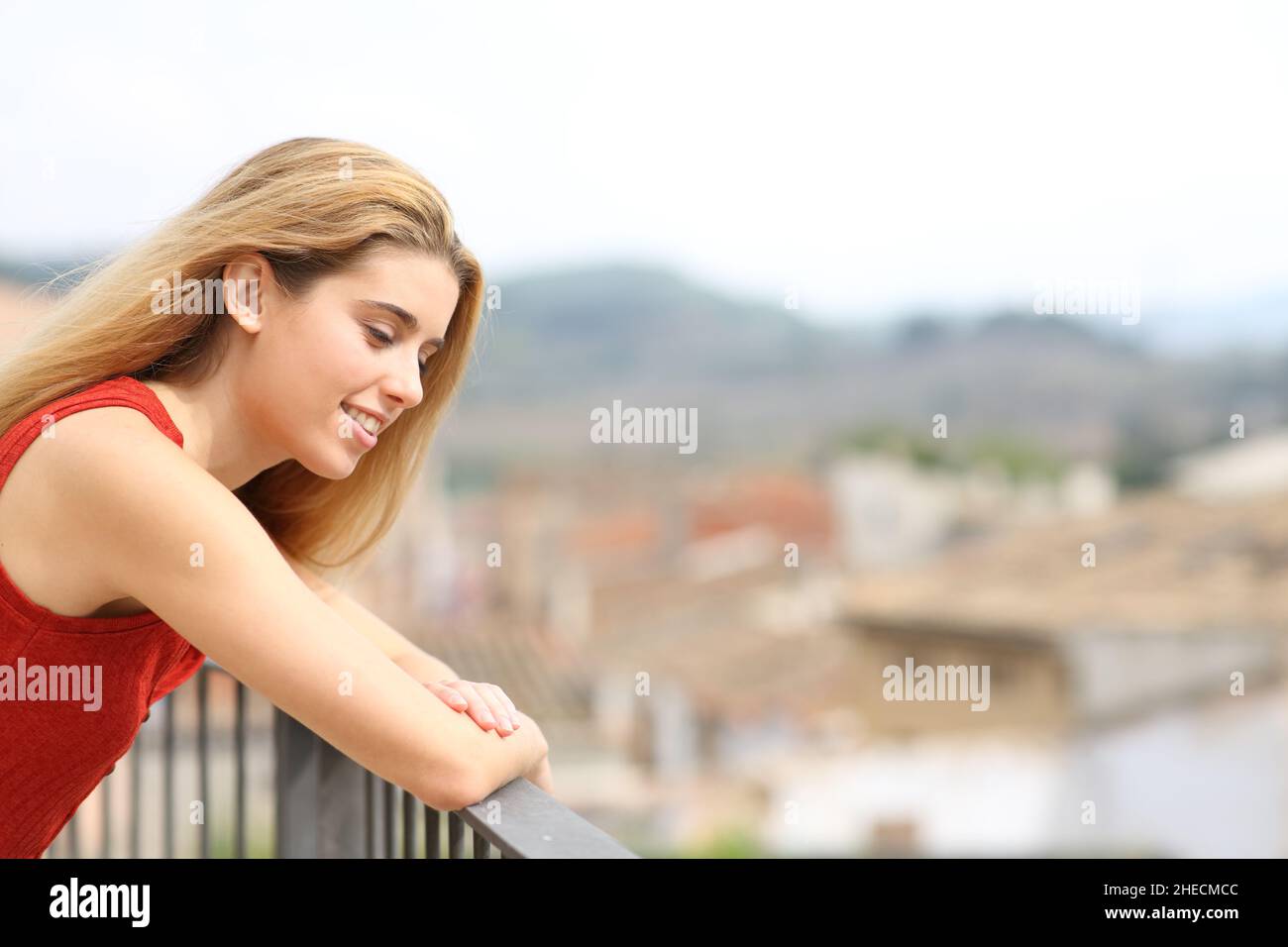 Happy woman looking down smiling in a balcony in a rural town Stock Photo