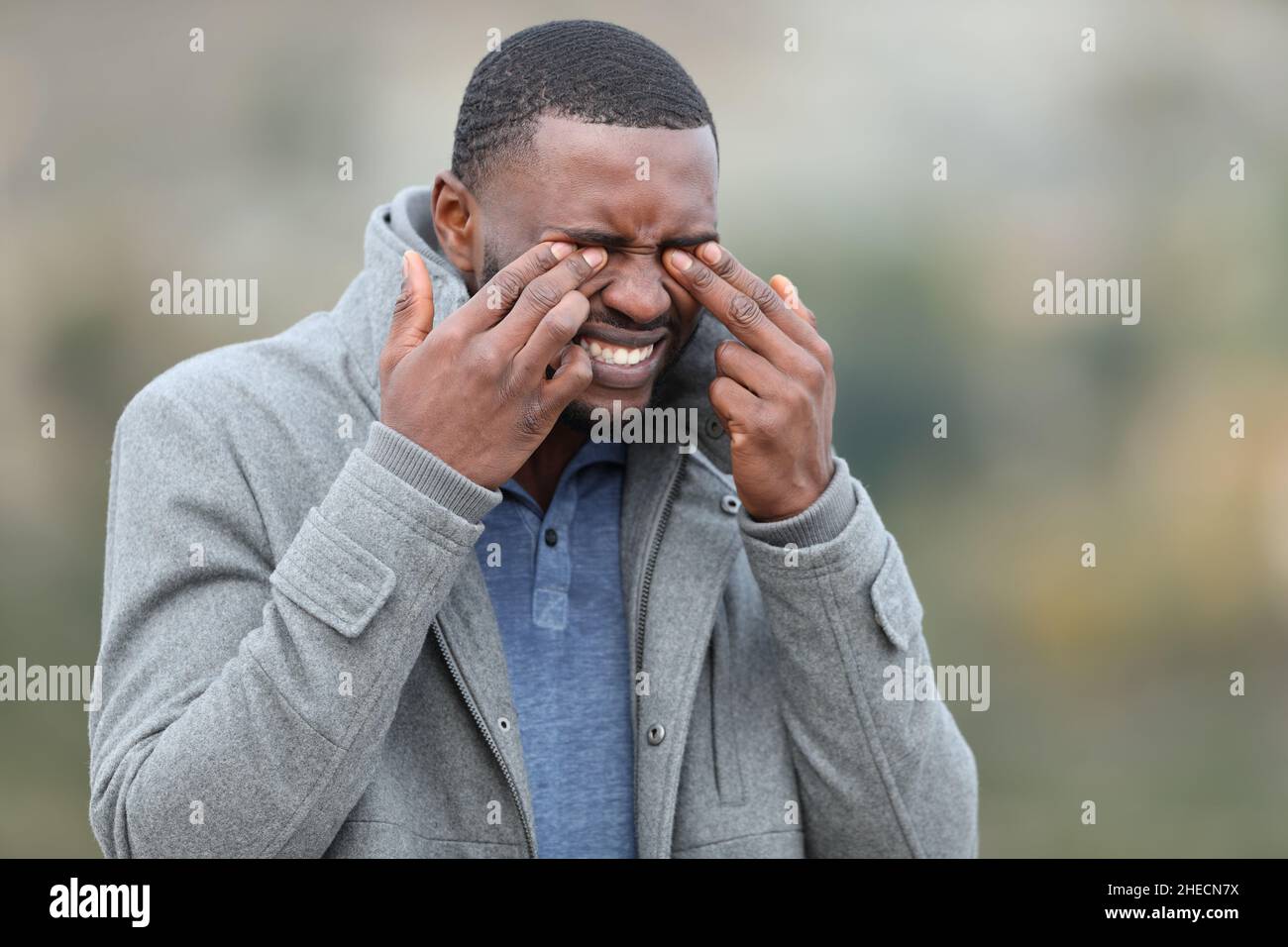 Stressed man with black skin scratching his eyes in winter Stock Photo