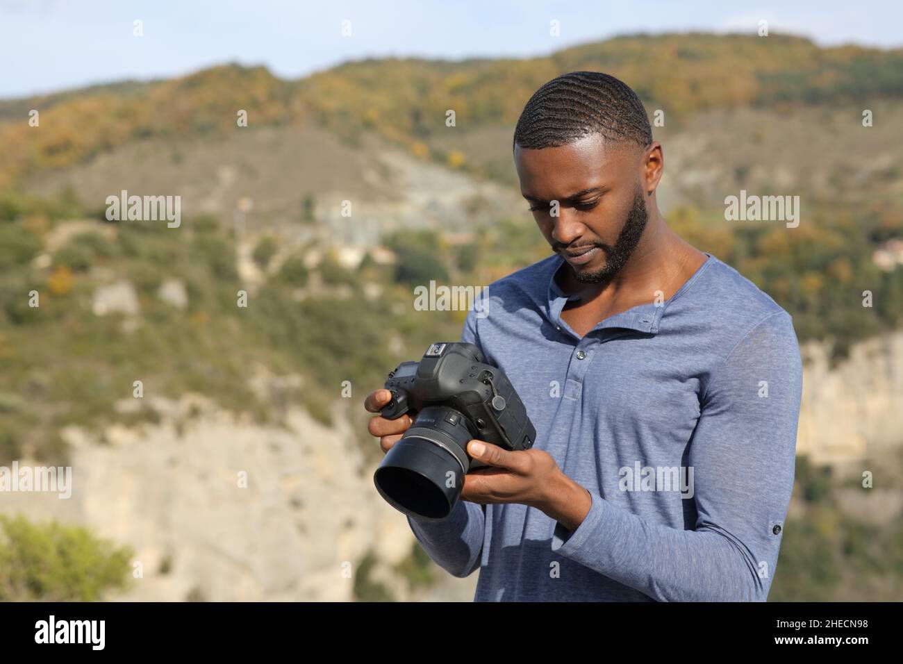 Concentrated man with black skin checking photos on dslr camera in nature Stock Photo
