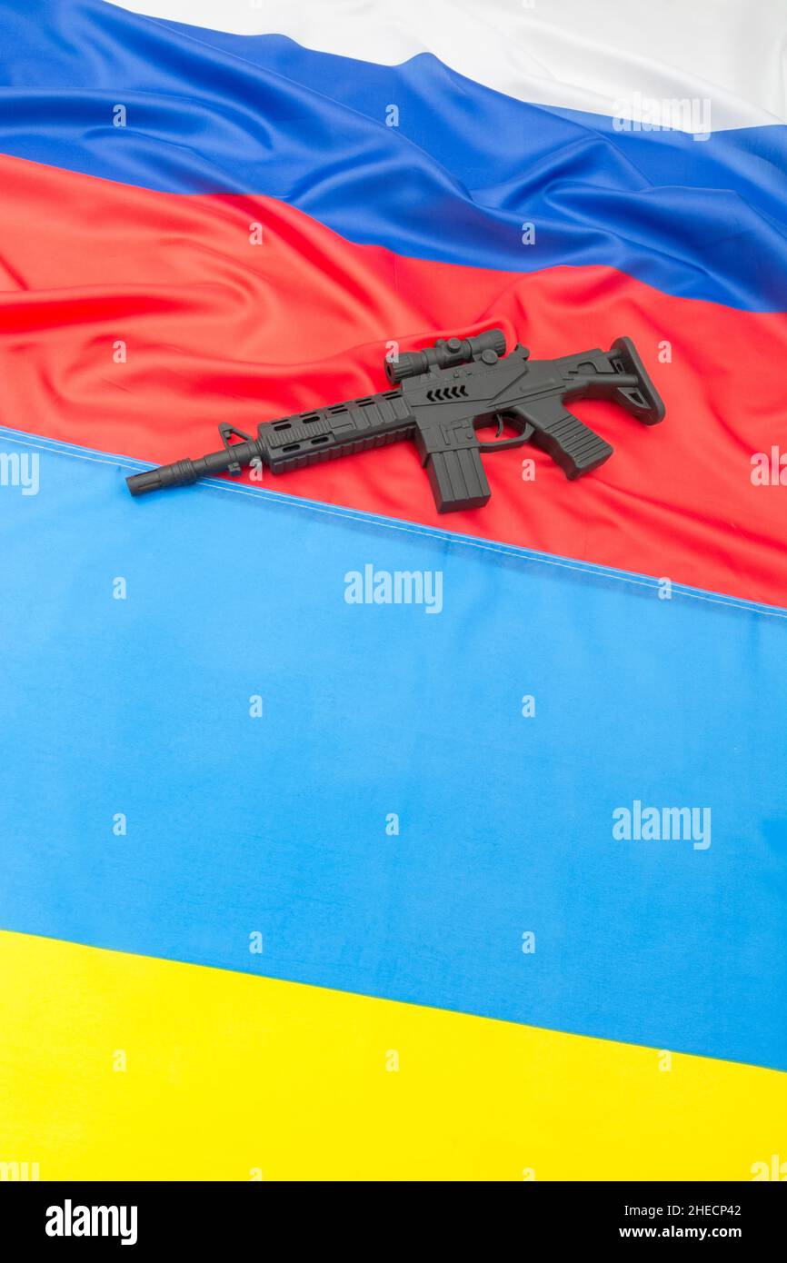 Russian & yellow blue Ukrainian flag + black painted toy assault rifle. For Ukraine-Russia crisis, Russia Ukraine invasion, tensions / war in Ukraine. Stock Photo