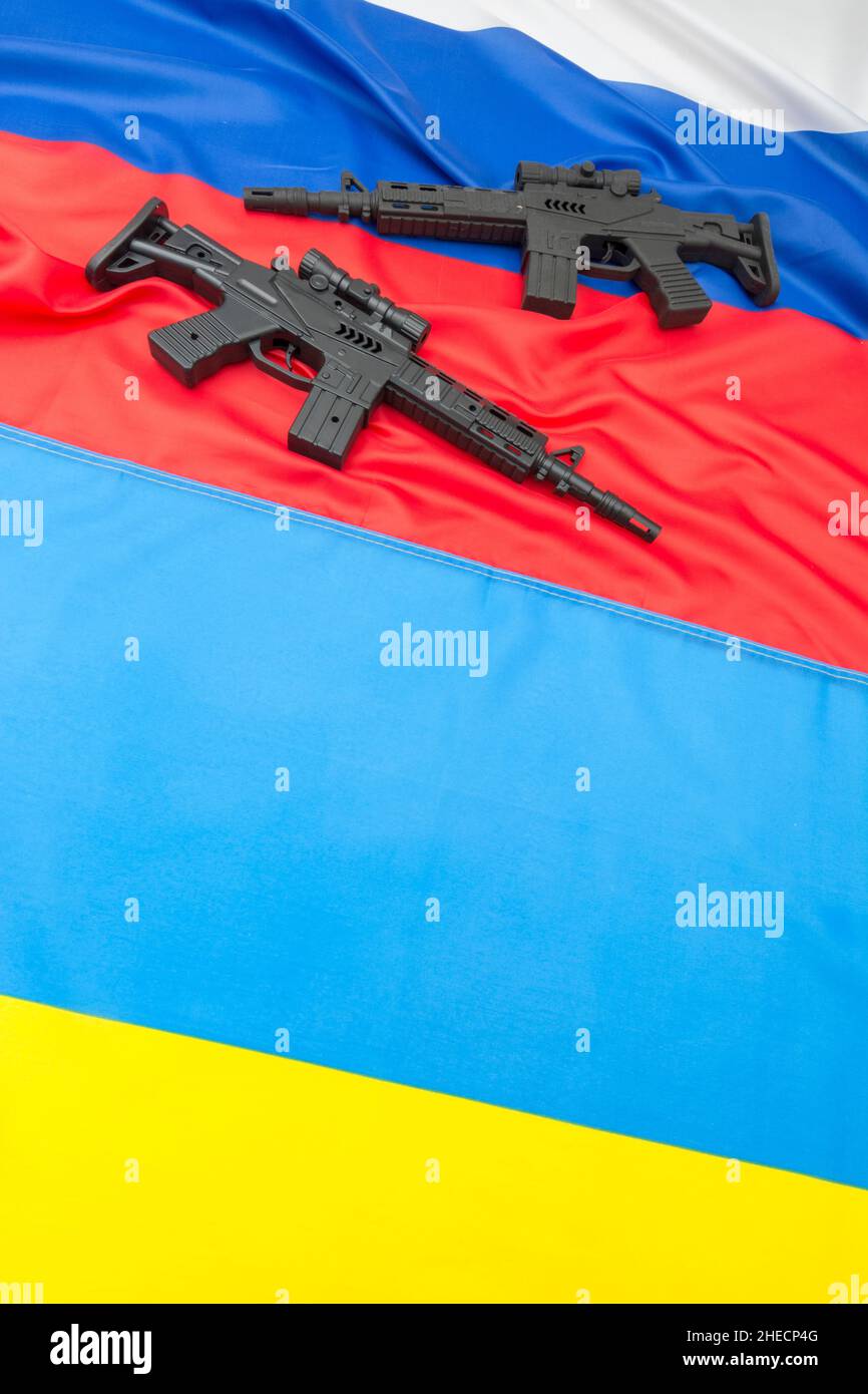 Russian & yellow blue Ukrainian flag + black painted toy assault rifle. For Ukraine-Russia crisis, Russia Ukraine invasion, tensions / war in Ukraine. Stock Photo