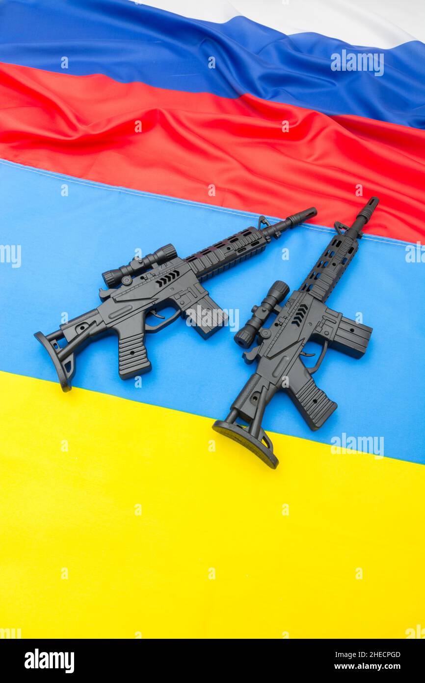 Russian & yellow blue Ukrainian flag + black painted toy assault rifle. For Ukraine-Russia crisis, Russia Ukraine invasion, tensions / war in Ukraine Stock Photo
