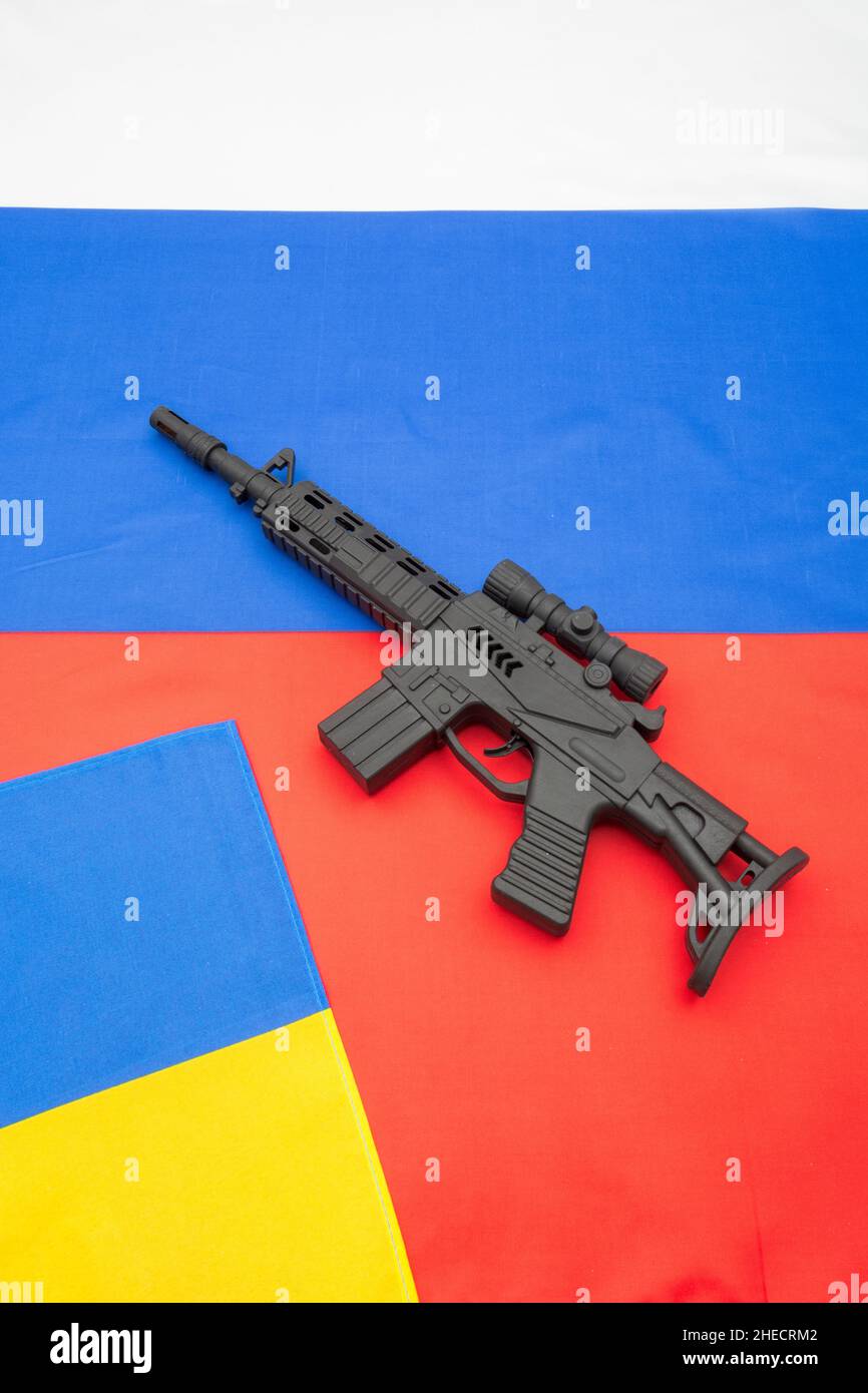 Russian & yellow blue Ukrainian flag + black painted toy assault rifle. For Ukraine-Russia crisis, Russia Ukraine invasion, tensions / war in Ukraine Stock Photo