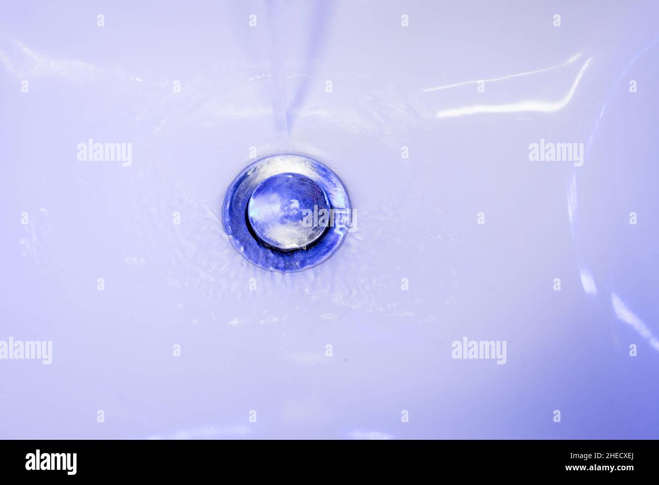 stream of clean water flows into in blue tones. Sink plug hole close up macro. Stock Photo