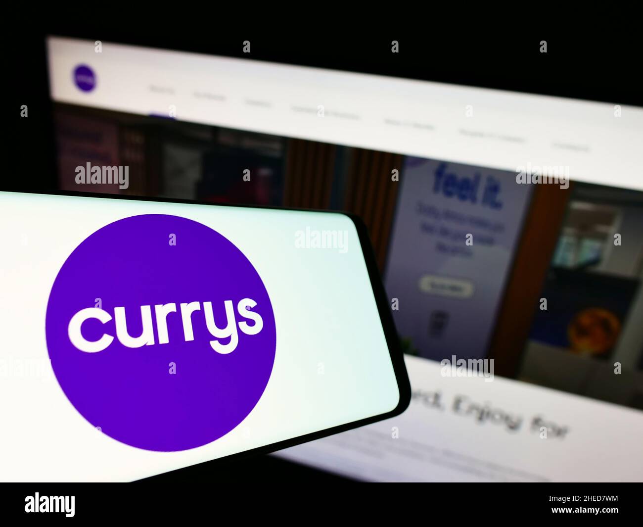 Smartphone with logo of British electronics retail company Currys plc on screen in front of website. Focus on center-right of phone display. Stock Photo