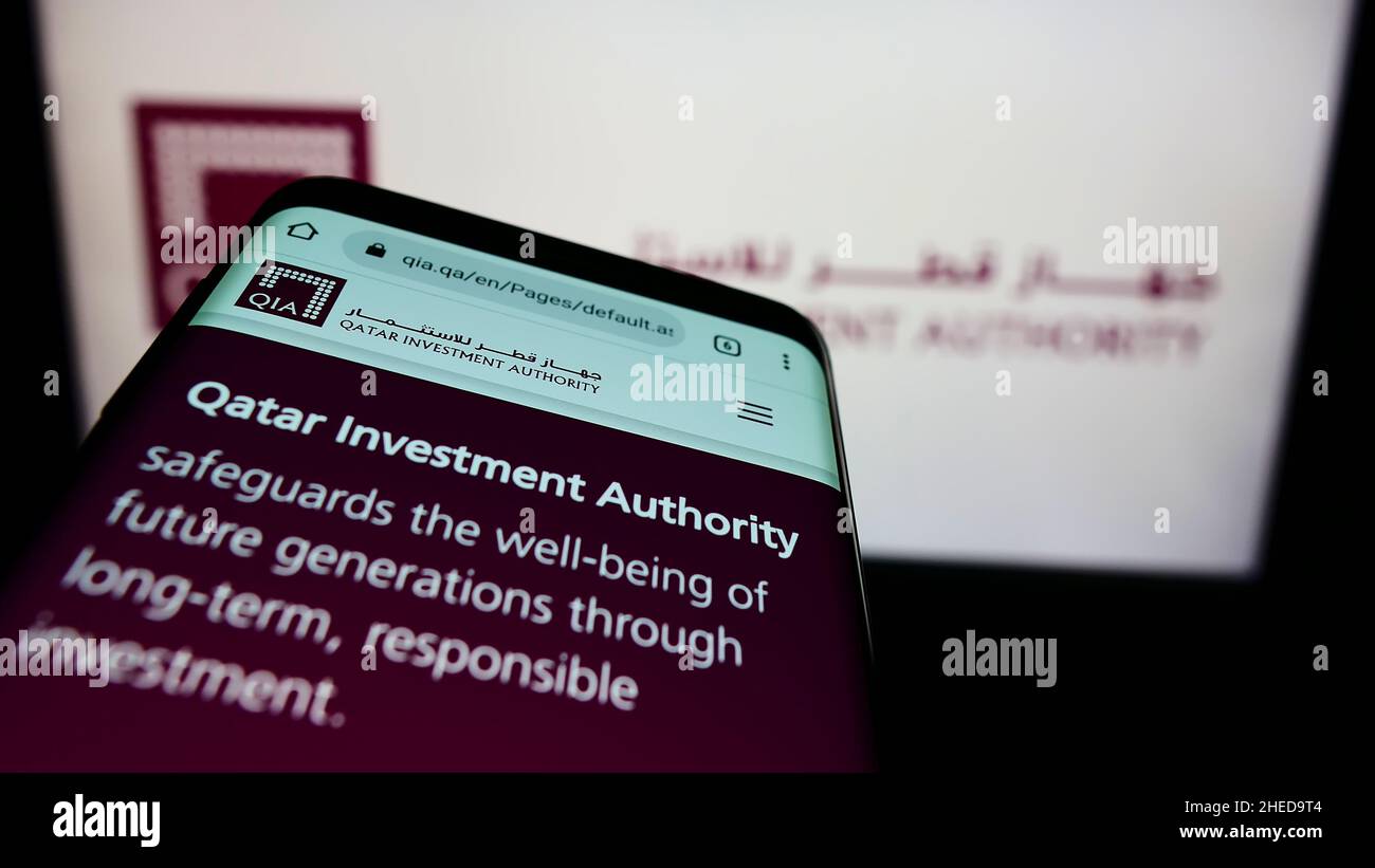 Smartphone with website of wealth fund Qatar Investment Authority (QIA) on screen in front of business logo. Focus on top-left of phone display. Stock Photo