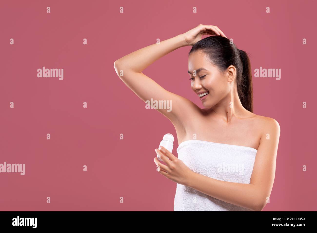 Smiling chinese woman using deodorant on purple background Stock Photo