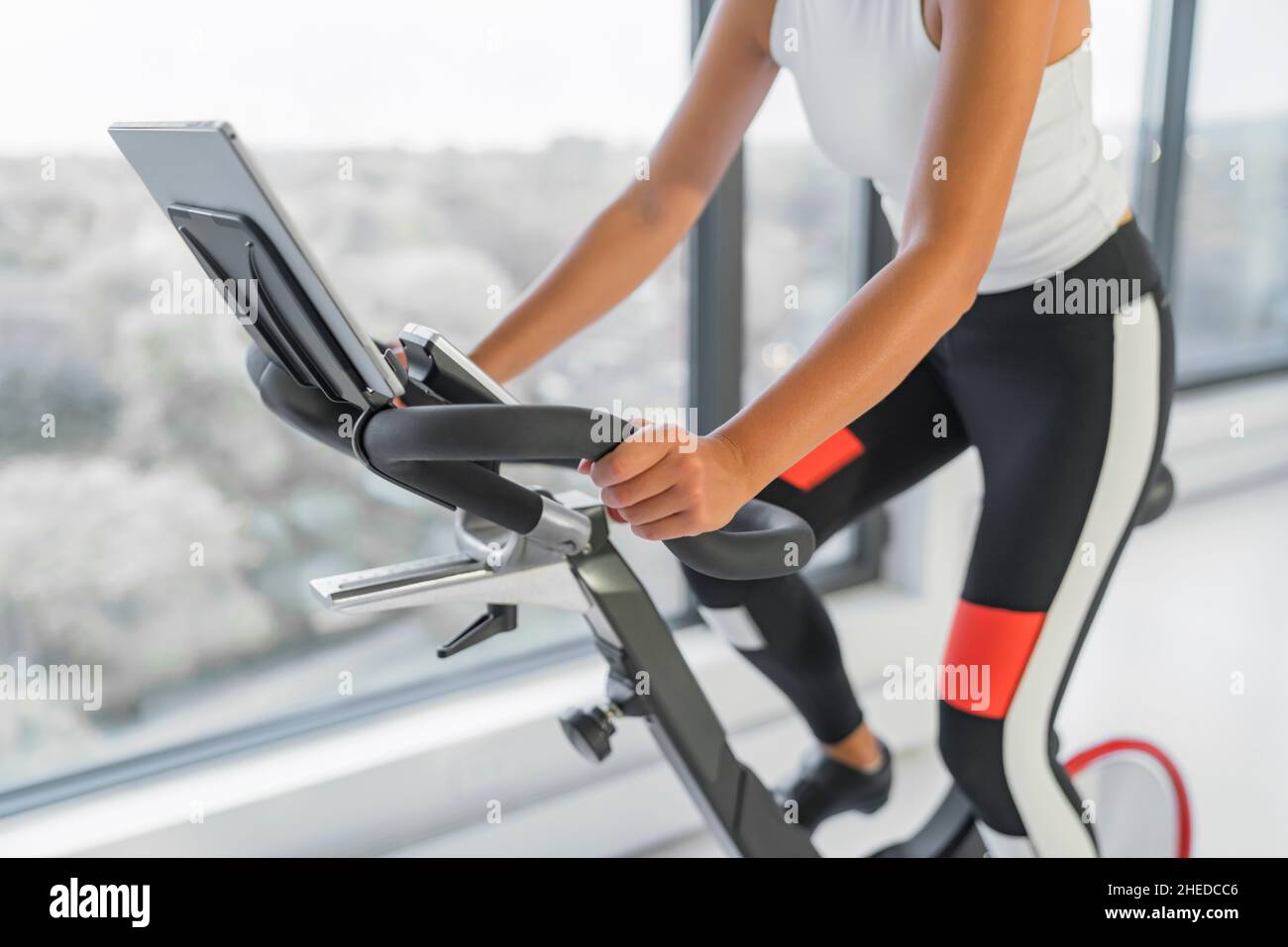 Exercise at home on spin bicycle fitness workout with screen. Woman training on stationary bike watching online video class for exercising cardio Stock Photo