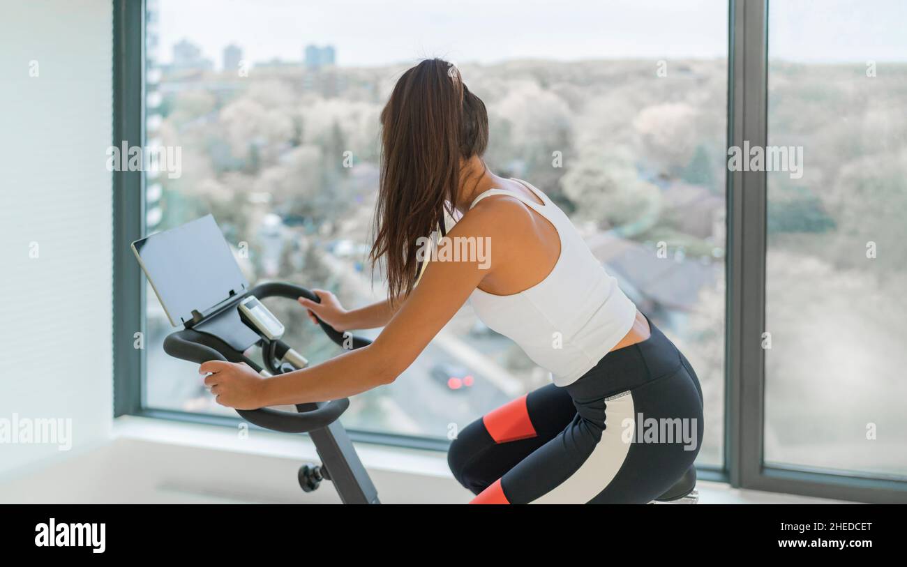 Home fitness workout woman training cardio on bike cyle with online gym class streaming. Girl biking on stationary bicycle indoor Stock Photo