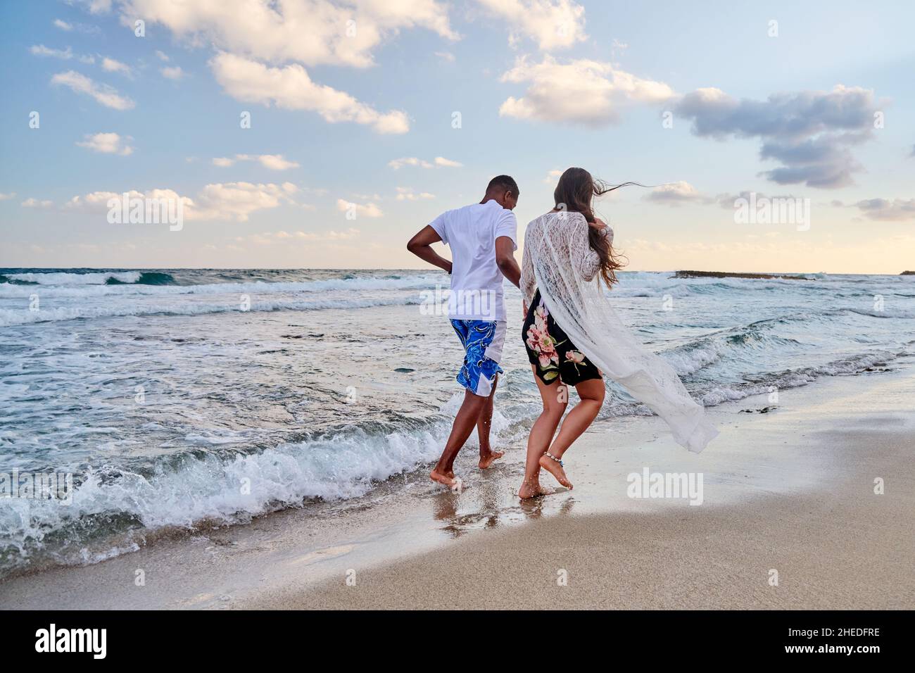 Happy couple running together on beach on summer day, back view Stock Photo