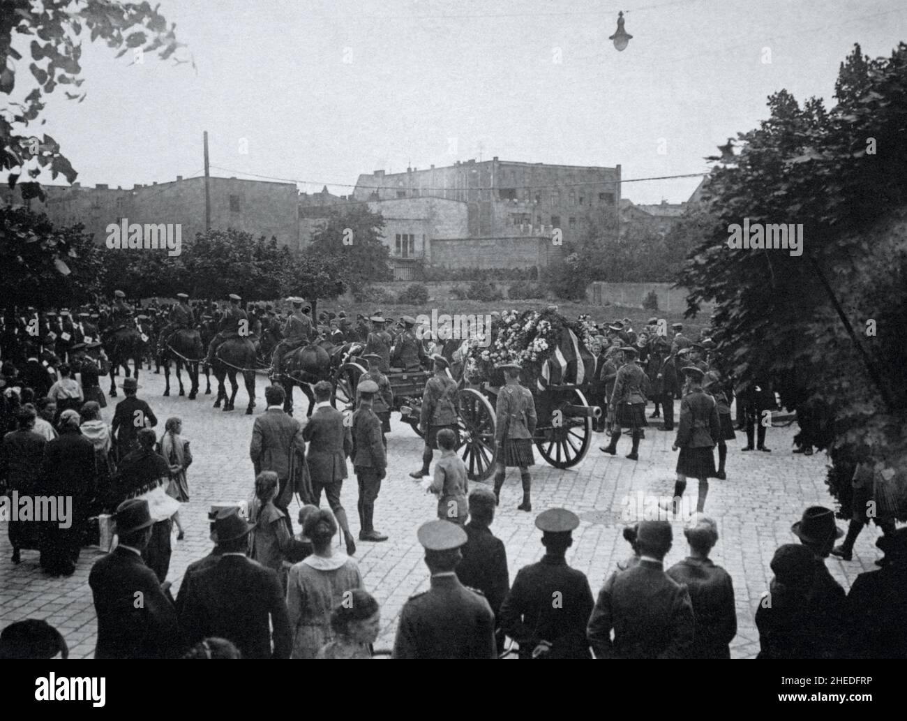 A historical view of a military funeral with the coffin drapped in a flag and pulled on a gun carriage. The coffin has a guard of honour of kilted Scottish infantrymen. Civilians and soldiers are watching the procession. Believed to be First World War era. Stock Photo