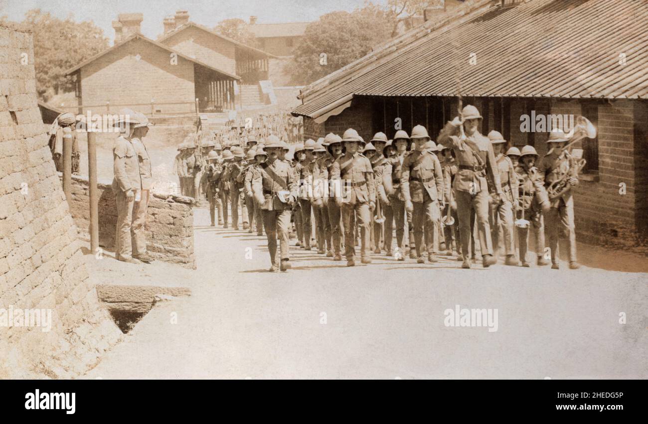 A historical view of a column of a British army infantry battalion marching with shouldered rifles and headed by a military band. The infantrymen are maching back though their barracks after attending church parade. They are in tropical uniforms and pith helmets. These troops are likely to have been garrisoning part of the British empire, possibly India. Pre-First World War era. Stock Photo
