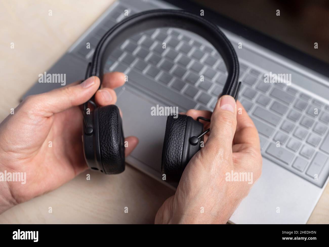 Headphones in hands and laptop. Listening to music and podcast concept. Stock Photo