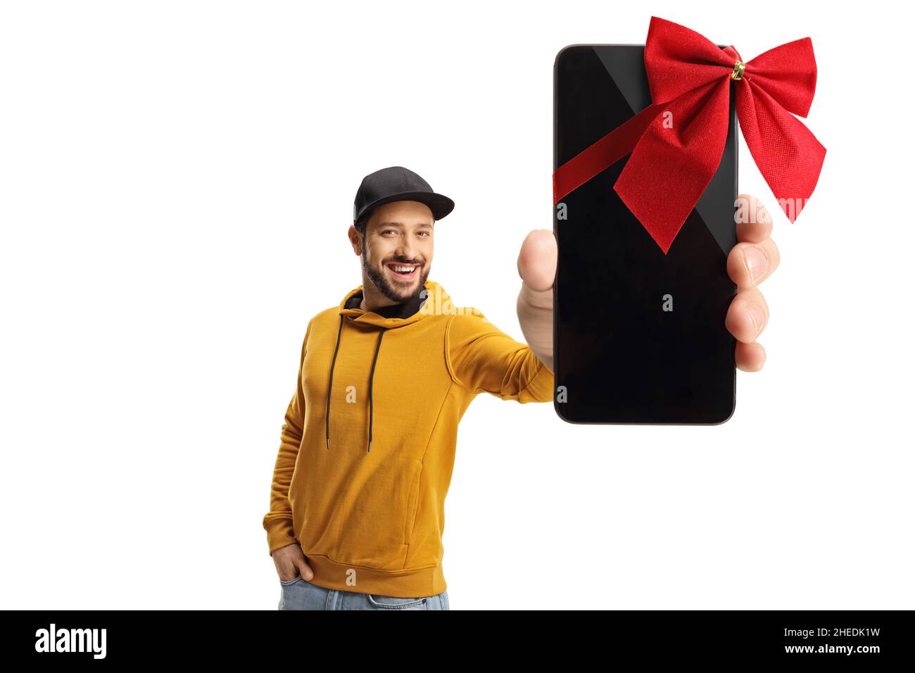 Cheerful young man with a yellow sweatshirt holding a smartphone with a red ribbon bow isolated on white background Stock Photo