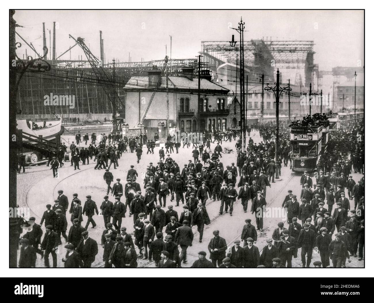 RMS Titanic under construction. Workers at shipyard at end of working day, ‘knocking off time’ from Harland & Wolff, Belfast. RMS Titanic is in background being constructed, being built by the crowds of ship workers. Belfast UK Date 1910 Stock Photo