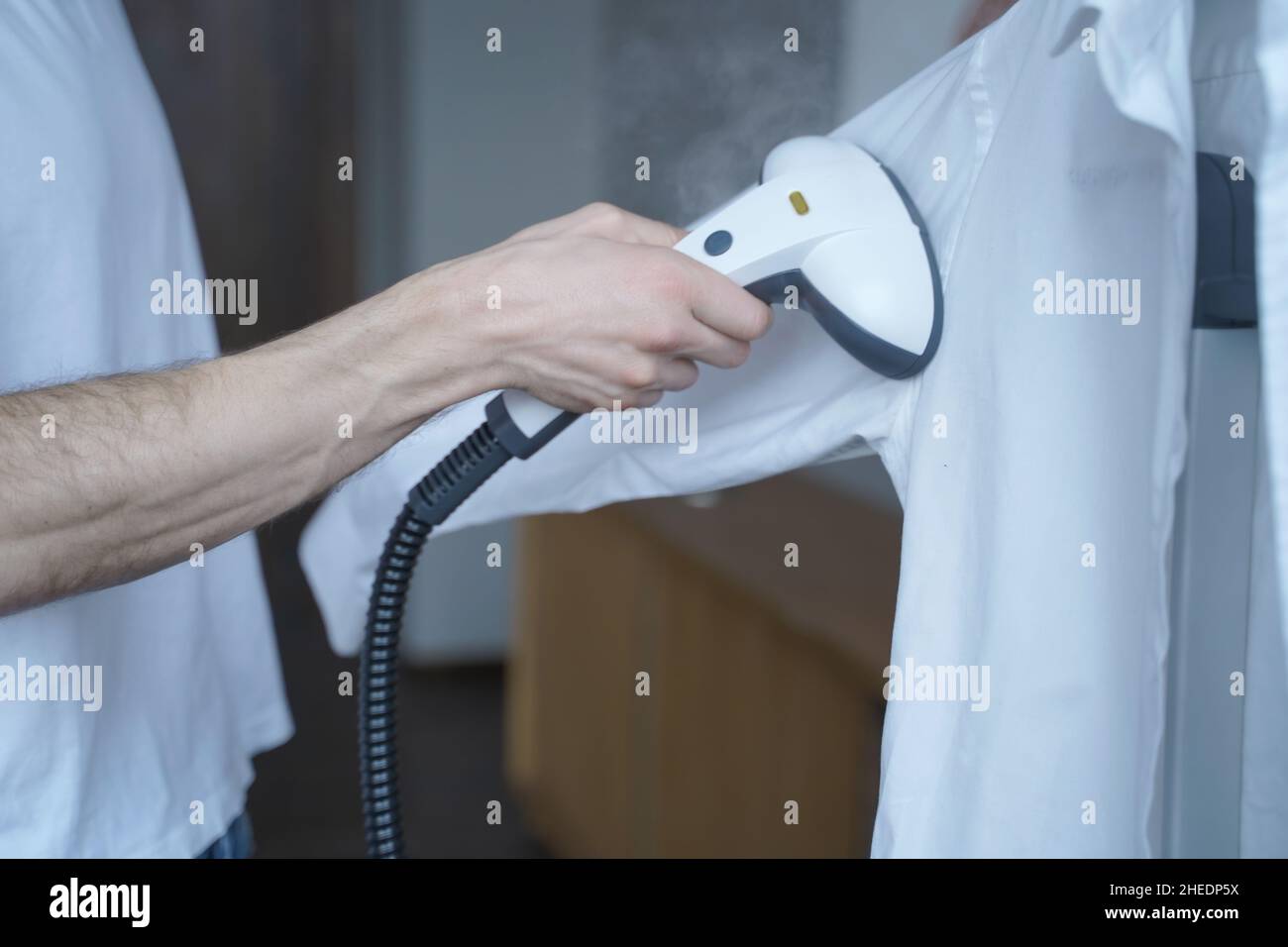 Cropped shot of man using electric garment steamer while steaming while classic shirt at home Stock Photo