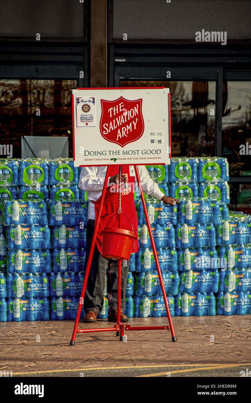 10-03 2021 Tulsa OK USA - Salvation Army bellringer (face hidden) in front of stacked packages of water bottles with hanging kettle on sidewalk at sto Stock Photo
