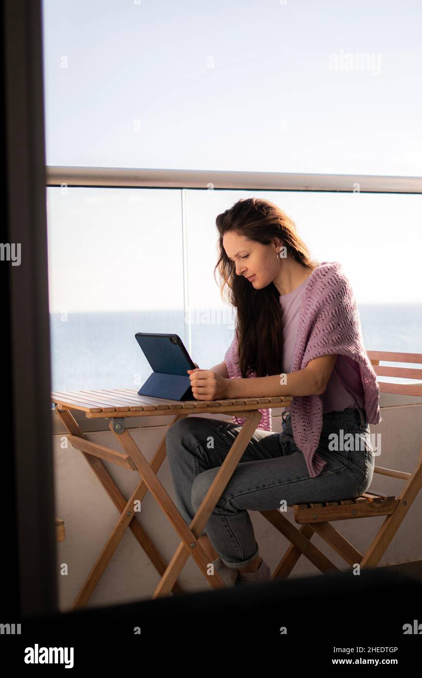 A young woman is working on tablet on the balcony near the sea Stock Photo