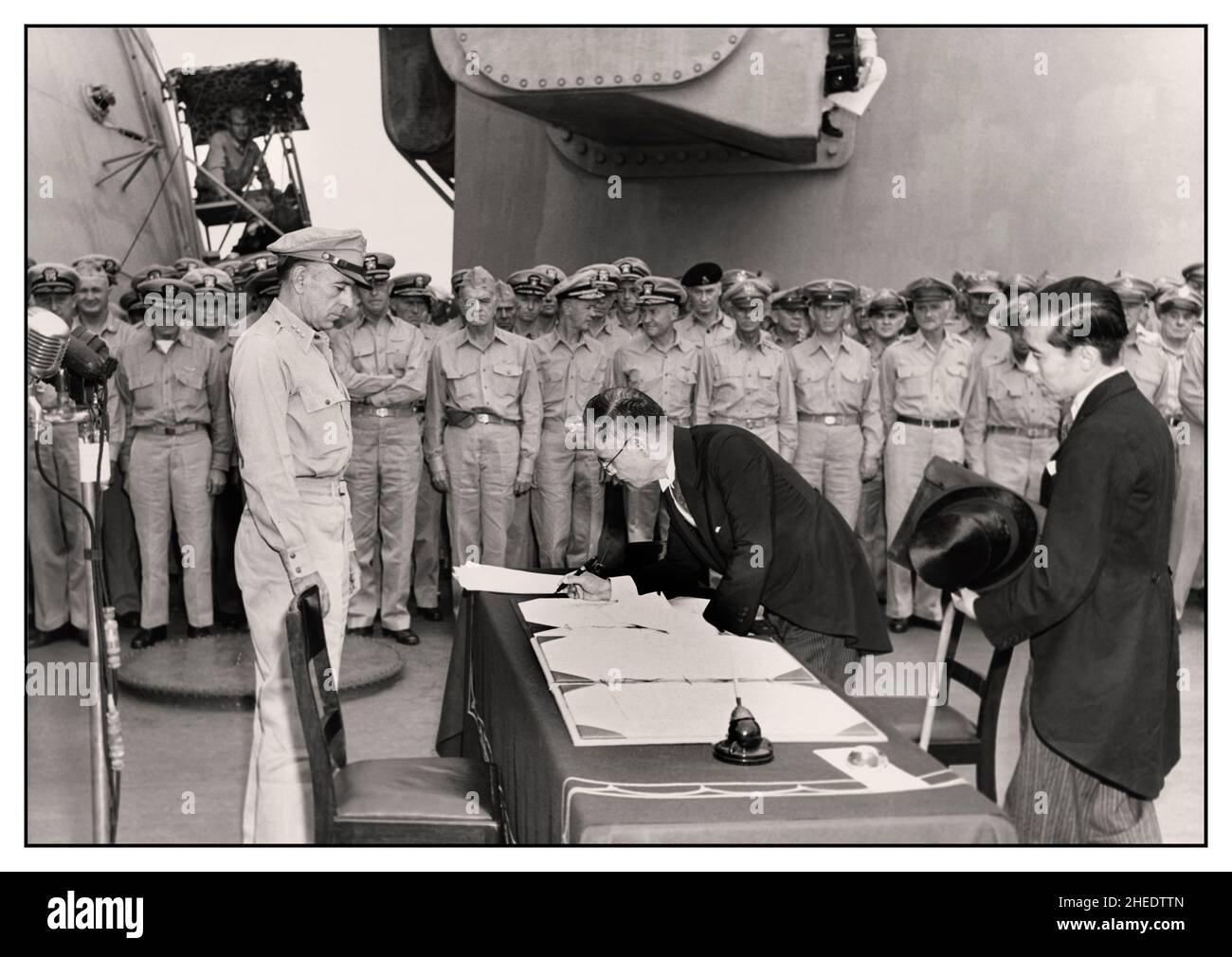 VJ Day World War II Victory over Japan Japanese Surrender. Japanese Foreign Minister Mamoru Shigemitsu signs the Instrument of  unconditional surrender on behalf of the Japanese Government, on board USS Missouri, 2 September 1945. Lieutentant General Richard K. Sutherland, U.S. Army, watches from the opposite side of the table. Foreign Ministry representative Toshikazu Kase is assisting Mr. Shigemitsu. Stock Photo