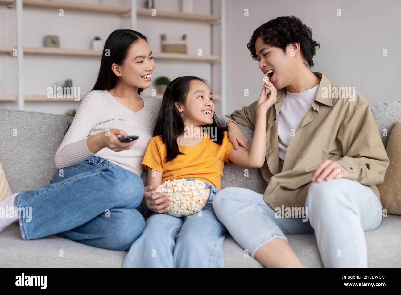 Cheerful young asian lady man and teenager girl watch tv daughter feeding daddy popcorn sits on sofa Stock Photo Alamy