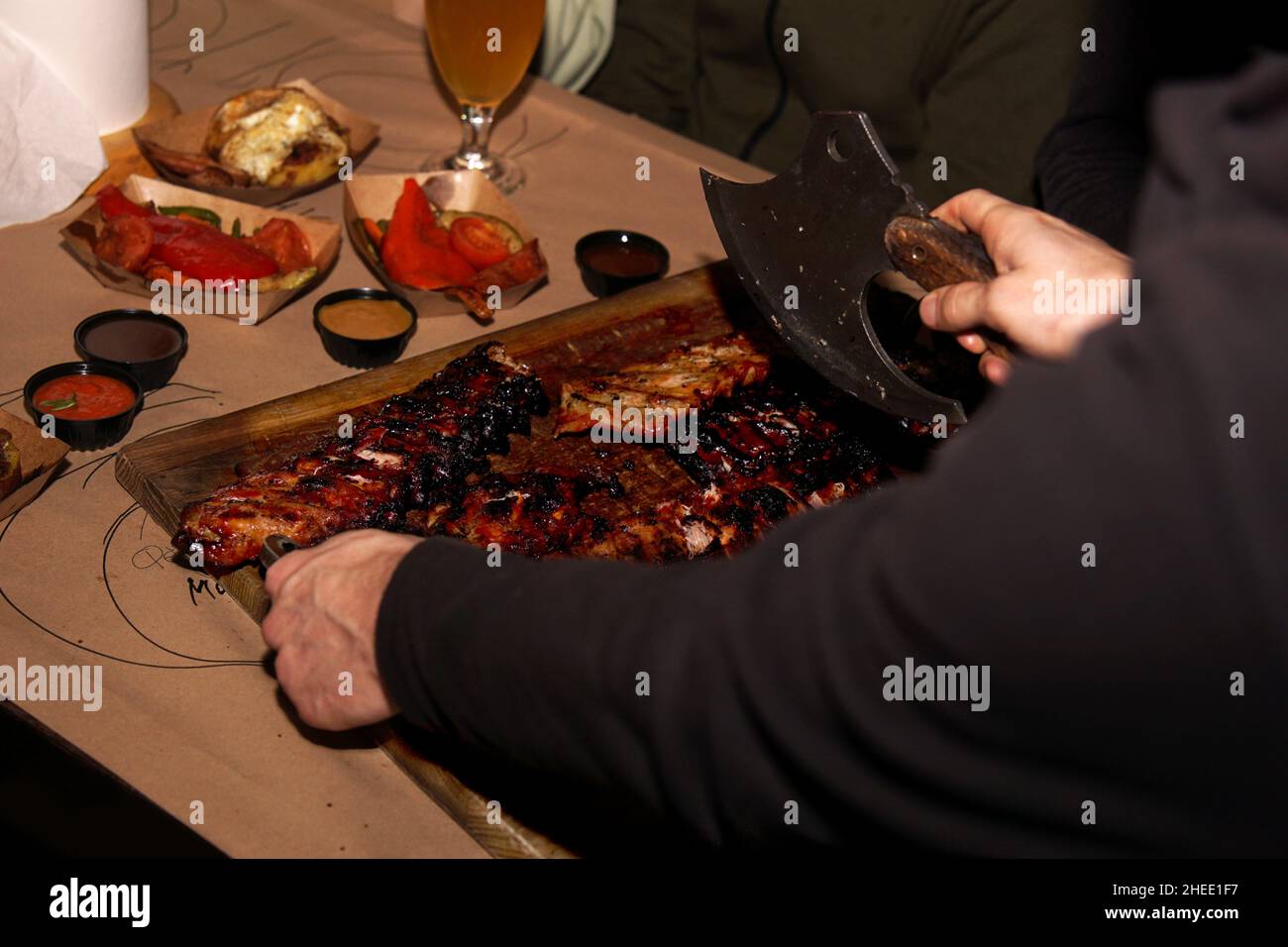 Waiter chops juicy barbecue ribs when serving to restaurant customers. Meat restaurant in Lviv