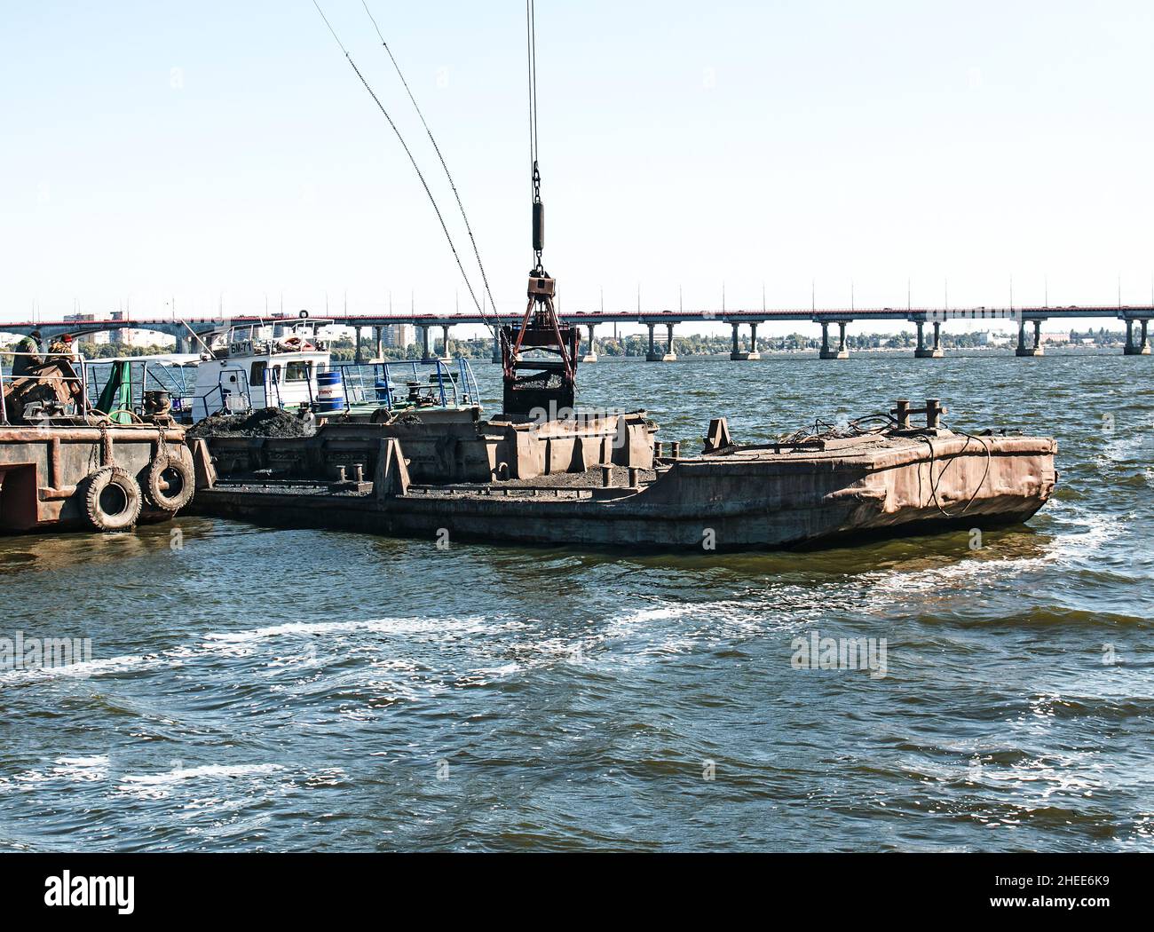 Cleaning the newly formed island from industrial waste on the Dnieper with a dredger. The bucket unloads the mud onto the barge. Ecology concept. Stock Photo