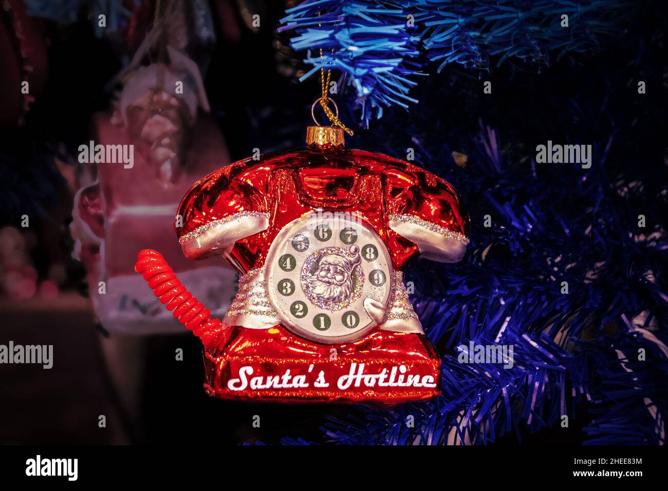 Santas Hotline red retro telephone ornament hanging on blue Christmas tree - Closeup and glittery on dark blurred background- Room for copy Stock Photo