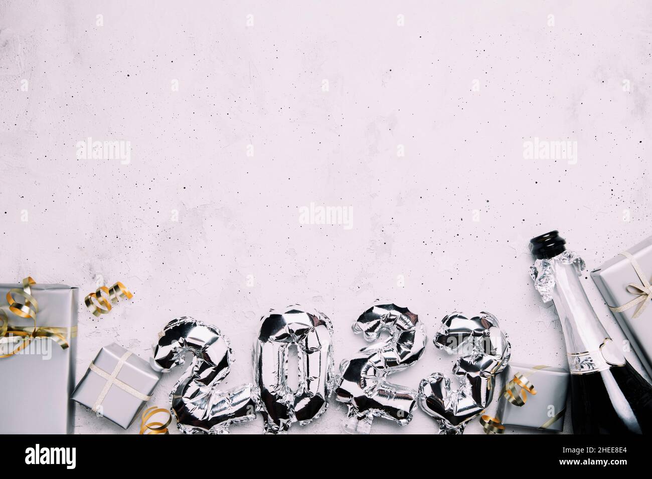 New Year 2023 gray background flat lay. Top view on 2023 balloon silver metallic numbers with grey gift boxes, golden ribbon. Invitation or greeting card. Festive mood. Opened champagne wine bottle Stock Photo