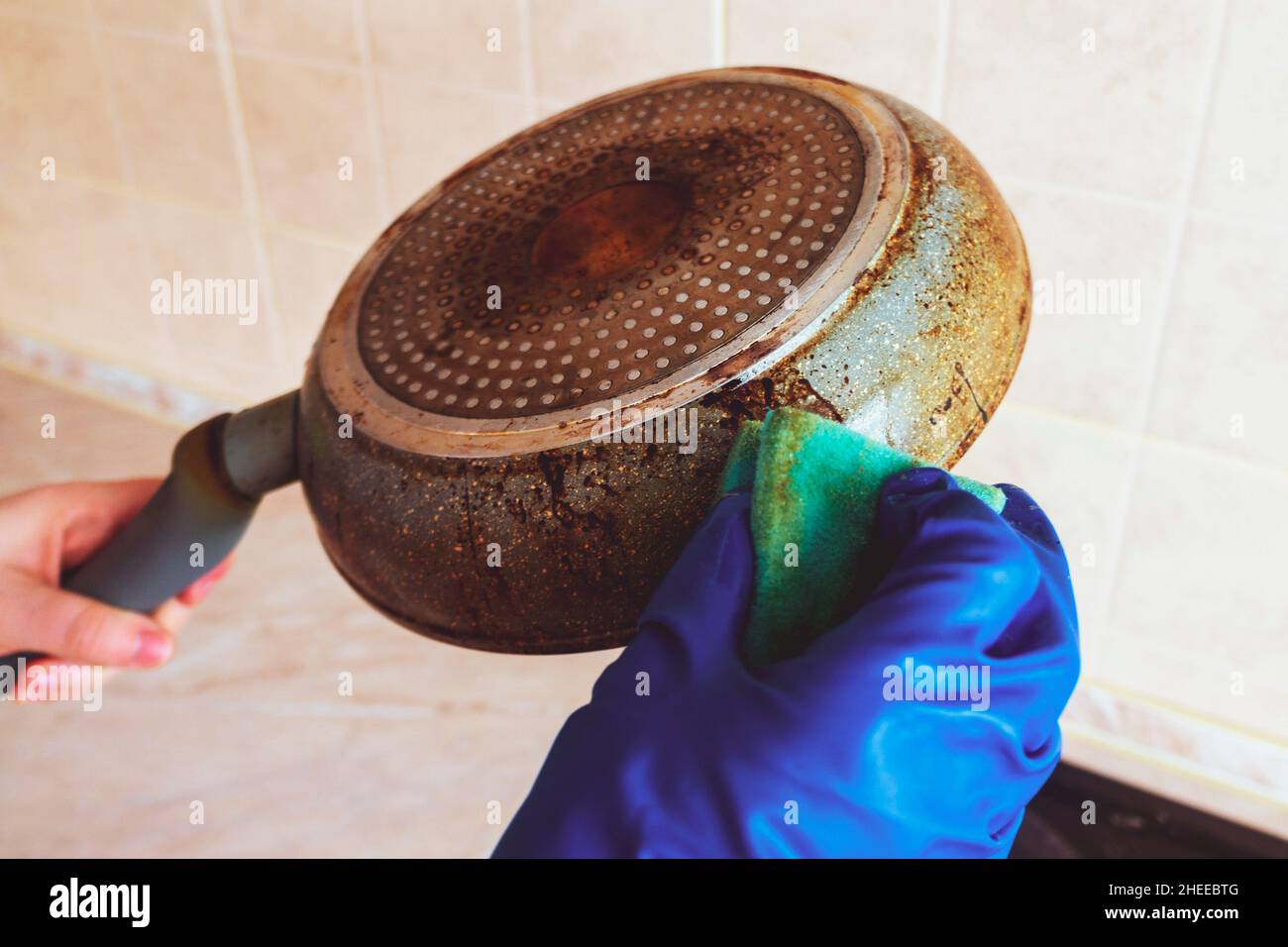 Cleaning a dirty frying pan with a kitchen sponge in the glove. Female