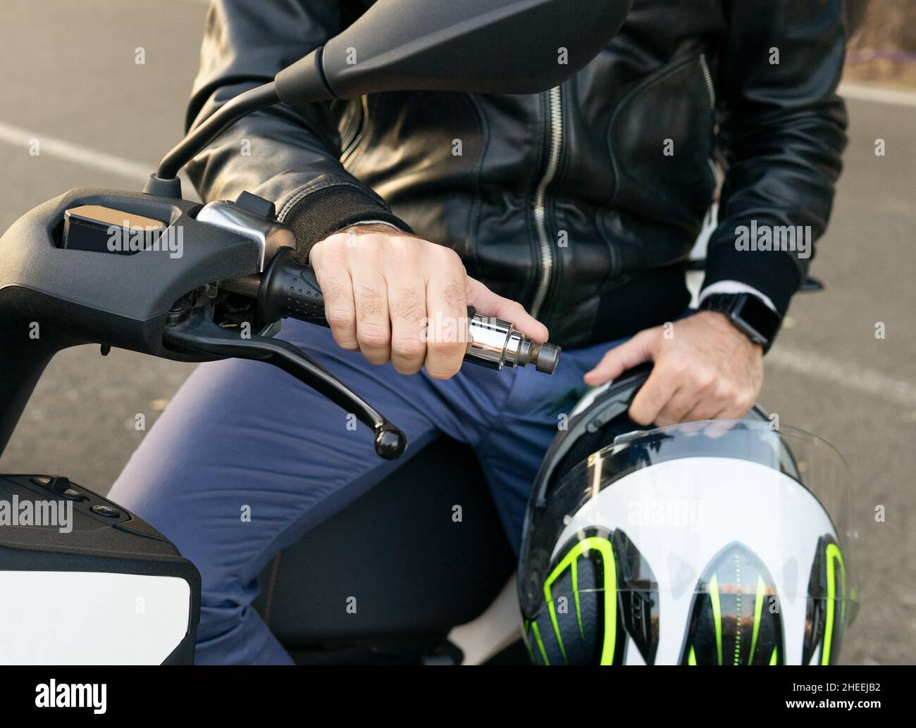 Cropped unrecognizable male biker in leather jacket sitting on motorbike parked on street near road in city Stock Photo