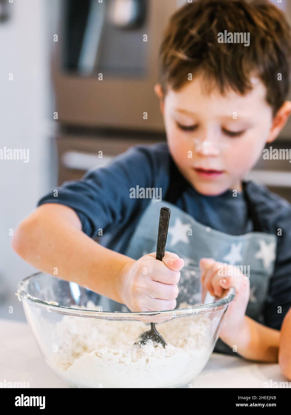Focused little kid with brown hair and in apron and with face covered