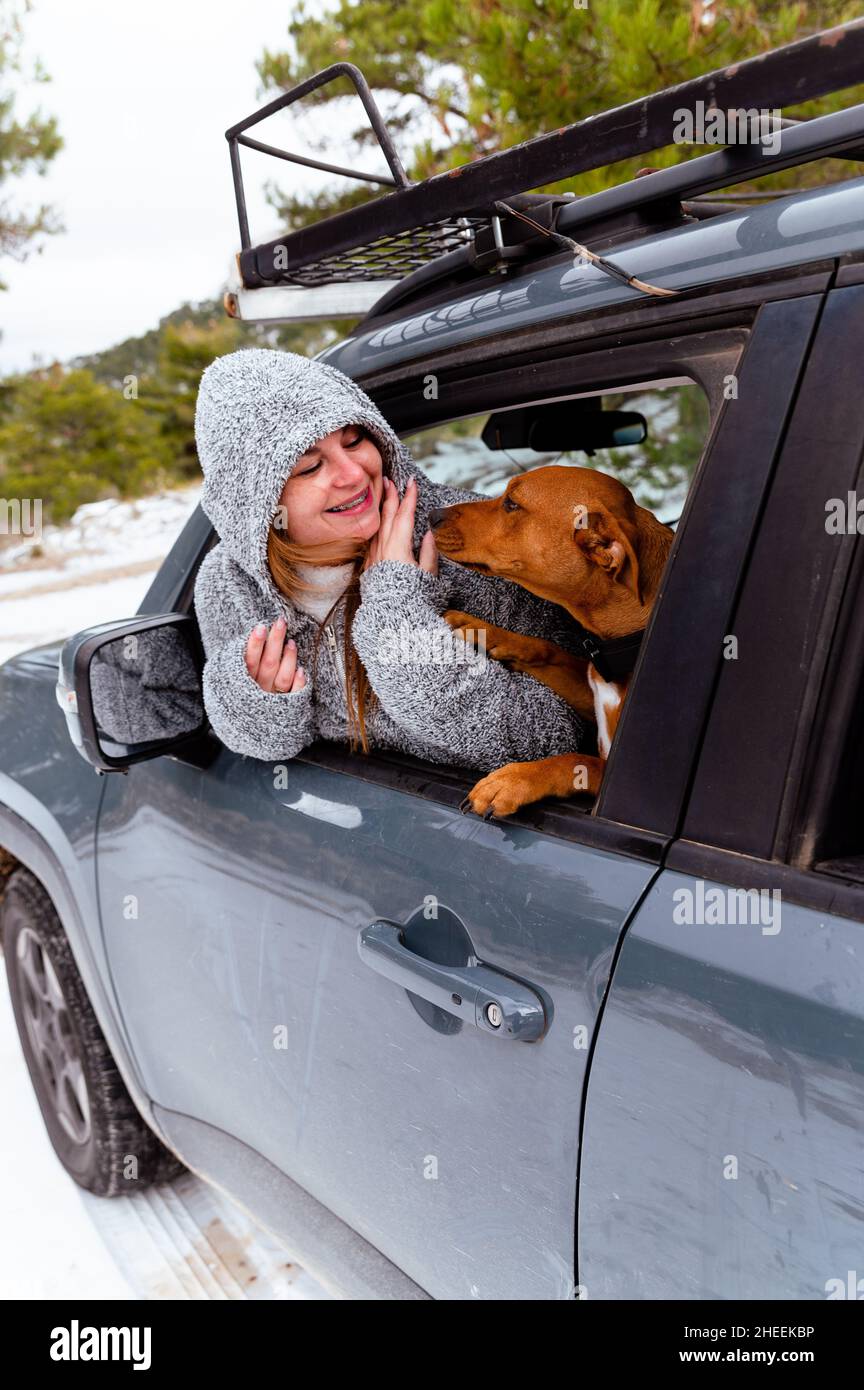 Woman sitting on driver seat caressing dog through opened window in parked car in frosty winter day Stock Photo
