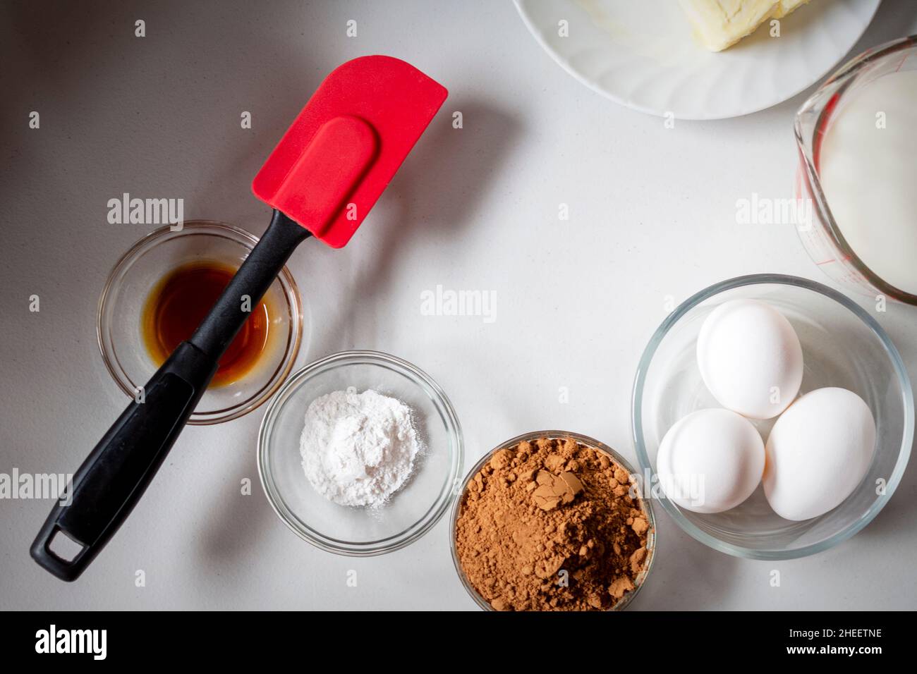 Looking down on some of the ingredients for baking a basic chocolate cake.  Ingredients include butter, milk, eggs, cocoa, baking powder, and vanilla. Stock Photo