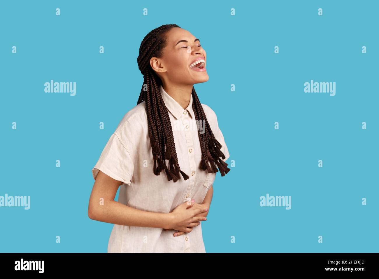 Portrait of happy beautiful woman with black dreadlocks laughing out loud, hearing funny joke, expressing positive, wearing white shirt. Indoor studio shot isolated on blue background. Stock Photo