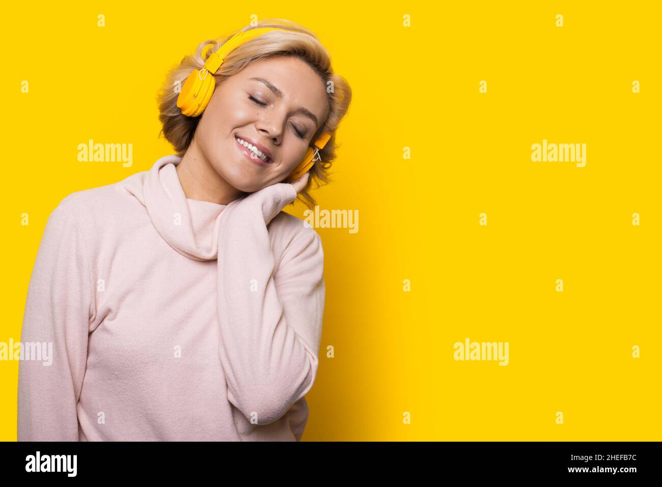 Caucasian woman in headphones enjoying music isolated over yellow background with copyspace. Closed eyes. Headphones music. Playlist listening. Song Stock Photo
