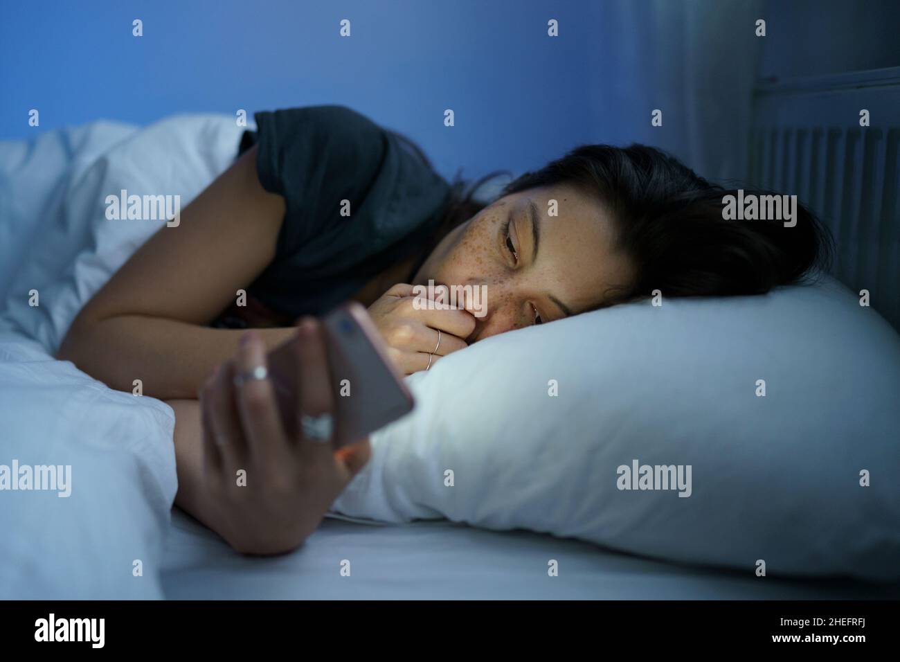 Anxious woman in bed using smartphone at night, can not stop scrolling