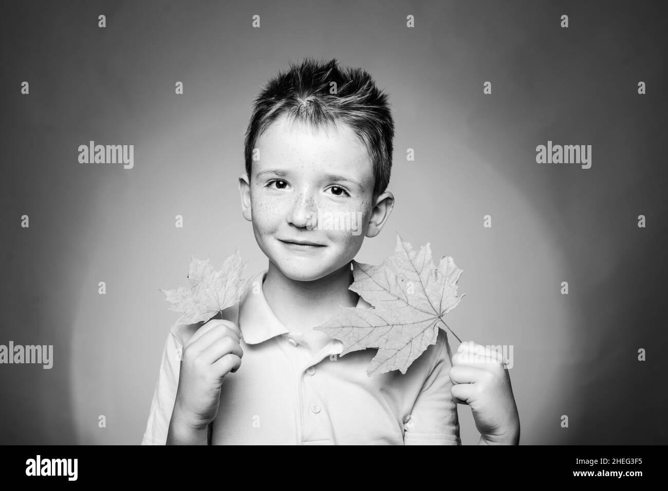 Red-haired kid boy playing with leaves and looking at camera. Family childhood lifestyle concept. Autumn time for Fashion sale. Close-up portrait. Stock Photo